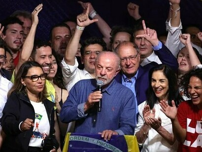 Lula aparece ao microfone, diante de uma tribuna coberta pela bandeira brasileira, enquanto as pessoas ao seu redor levantam os braços e celebram. A presença de apoiadores de diferentes perfis compõe uma imagem de entusiasmo coletivo, na qual a comemoração da vitória se transforma em manifestação pública de confiança política. Mas o significado histórico de uma eleição também se mede pelo que vem depois dela. Ao discutir o Brasil, o mundo e o futuro, Boaventura de Sousa Santos propõe olhar para além do resultado imediato: a defesa da democracia requer enfrentar o autoritarismo, combater as desigualdades e construir formas mais amplas de participação política. A mobilização retratada na imagem expressa uma força que precisará encontrar continuidade na vida democrática