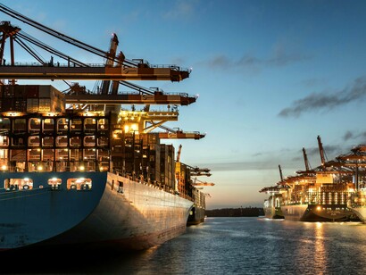 Cranes towering above loaded cargo ships, symbolising the competition for control over trade routes