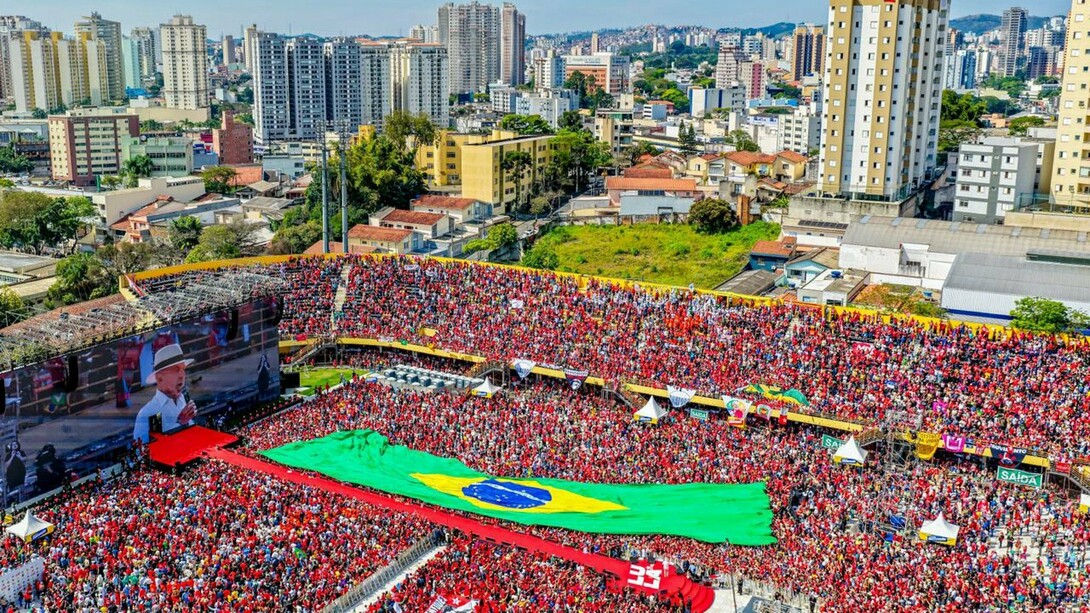Na Vila Euclides, em São Bernardo do Campo, Lula retorna ao lugar que marcou o início de sua trajetória política para lançar sua campanha à reeleição. Diante de uma multidão que ocupa o estádio, uma gigantesca bandeira brasileira se estende pelo campo, enquanto a cidade se abre ao fundo. A imagem condensa décadas de história política brasileira e coloca em primeiro plano a disputa por um país cuja democracia, como argumenta Boaventura de Sousa Santos, volta a estar no centro de uma escolha que ultrapassa os limites de uma eleição