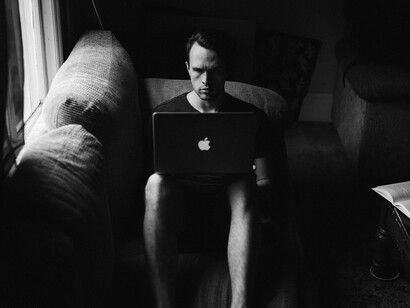 Homme assis sur le canapé utilisant un MacBook à côté de la fenêtre