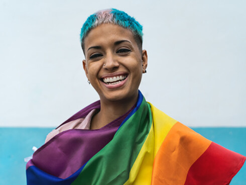 Young activist smiling and holding a rainbow flag, symbol of the LGBTQIA+ social movement