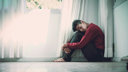 A barefoot young man hugging his legs, trying to sooth himself