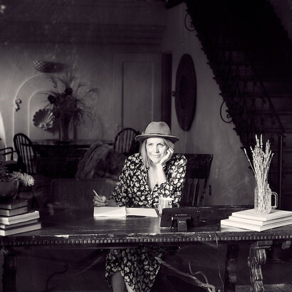 A timeless black and white photograph reveals a captivating scene—a gifted woman author, adorned with a chic hat, absorbed in her craft, gracefully seated on a chair, her writing capturing her thoughts and imagination, an embodiment of creativity and literary grace