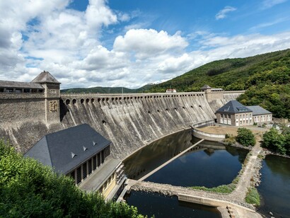 A vast dam spanning a mountainous landscape, symbolizing the power of public infrastructure to serve long-term collective needs