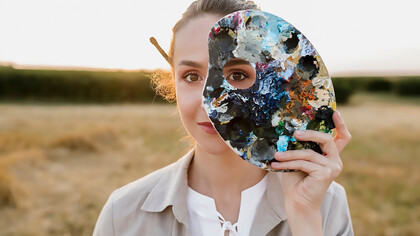 A creative young woman holding a painting palette, inspired by the connection between art and dreams, surrounded by surreal imagery