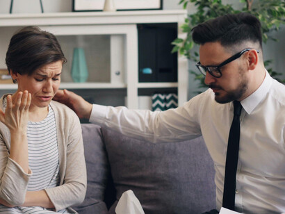 A man and a woman sitting on a couch, with the woman engaged in a therapy session