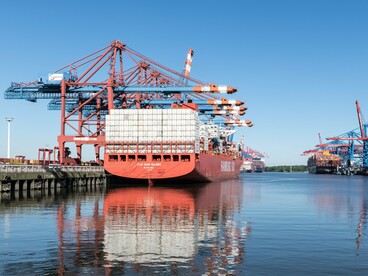 A cargo vessel surrounded by towering stacks of containers and cranes, symbolizing the scale of international commerce