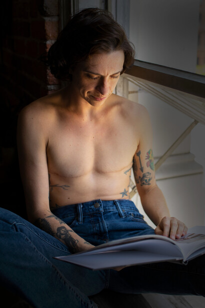 Homem lendo. Ele foi desabotoando a camisa com a sua mão direita com um vagar excepcional, enquanto, com a sua mão esquerda segurava um livro de poemas de Florbela Espanca que ia declamando