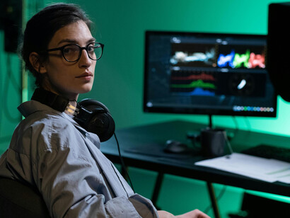 A woman sitting at her desk, working across multiple computer screens — a visual metaphor for digital overload, information excess, and the multitasking demands of the modern tech era