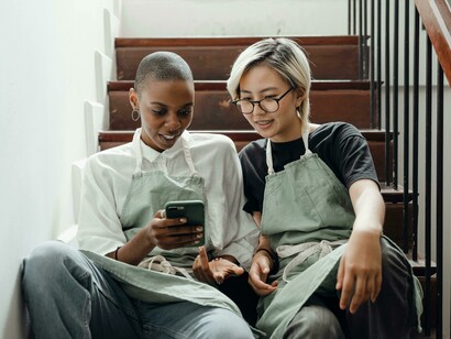 Colleagues in aprons sitting on a staircase and browsing smartphones while scrolling through social media   