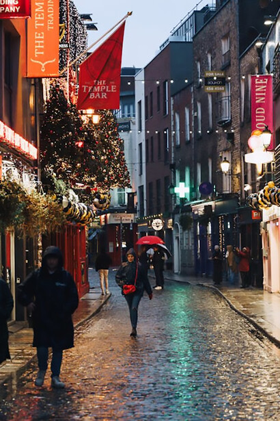 Rainy evening in Dublin’s Temple Bar, where people stroll with umbrellas under glowing Christmas lights