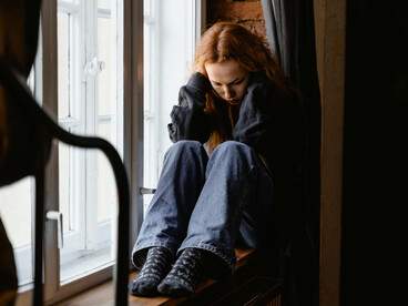 Stressed woman sitting on the window sill, lost in thought