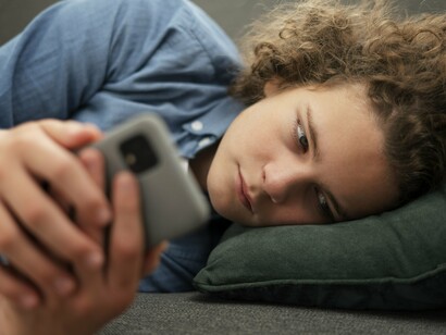 Adolescente utiliza o celular sozinho no sofá enquanto navega pelas redes sociais. A exposição contínua a estímulos extremos pode impactar empatia, impulsividade e percepção de risco. O ambiente doméstico nem sempre revela o que acontece nas telas. Muitos conteúdos violentos circulam silenciosamente nos espaços digitais frequentados por jovens