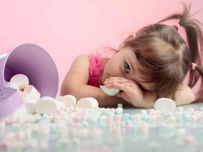 A charming little girl surrounded by a table full of marshmallows, set against a soft pink background