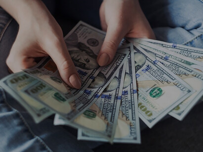 Grasped in their hand, a person holds a fan of U.S. dollar banknotes, embodying a visual representation of monetary abundance and financial resources