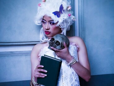 Em um retrato de inspiração clássica, uma mulher segura uma caveira diante do rosto. A imagem remete à atmosfera de Hamlet, de Shakespeare, e à presença recorrente da morte e da dúvida na literatura