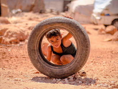 Playing in the dirt of a refugee camp in Syria, a child's smile contrasts sharply with the headlines of war and political upheaval, highlighting his and others' enduring spirit
