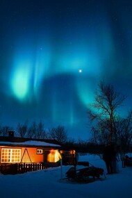 A brown cottage beneath a glowing aurora borealis