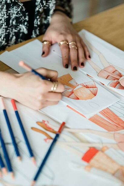 Uma mulher desenhando uma peça de roupa em uma mesa de trabalho. Desenhar moda é construir conceitos que irão dialogar com o mundo contemporâneo