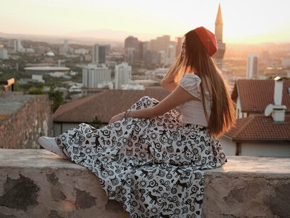 A woman quietly overlooking the city skyline at sunset, representing the silent conflict between outward ambition and inner contentment