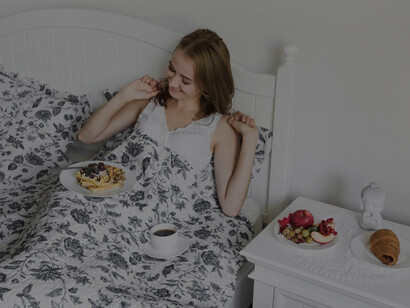A young woman enjoys a nutritious breakfast in bed, emphasizing the importance of diet and nutrients for a healthy sleep