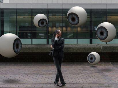 A person stands outdoors surrounded by symbolic eyes, representing the intersection of AI and surveillance, data privacy concerns, and Crime Prevention Through Environmental Design
