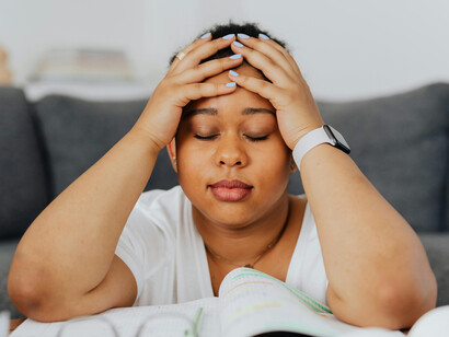 A female student in a white shirt holds her head in her hands, showing signs of burnout