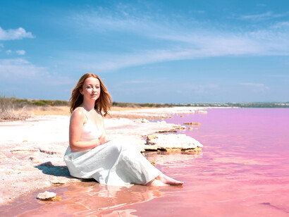 A woman in a white dress walks across a stunning pink lake