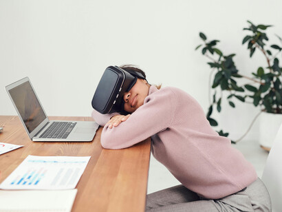 Una mujer descansa sobre su escritorio mientas ve videos en sus lentes de realidad virtual