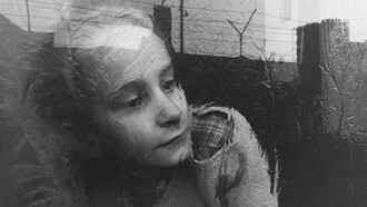 Una niña mira pensativa a través del cristal de la ventana de su apartamento, que refleja la imagen de la cerca de alambre de púas que corona el Muro de Berlín, en diciembre de 1962