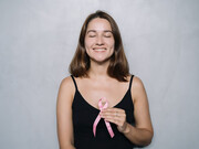 A woman wearing a black spaghetti strap top holds a pink ribbon, symbolizing breast cancer awareness