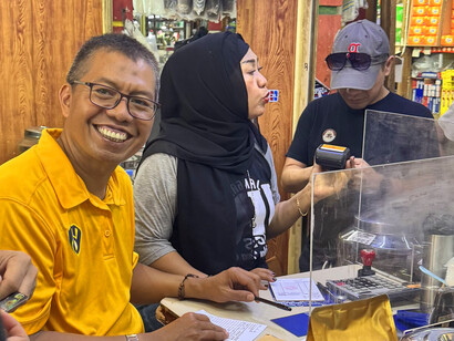 Mr. Suradi enjoys a moment of peace and pride as he oversees the bustling energy of Dunia Kopi, where the aroma of freshly brewed coffee fills the air