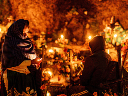 People celebrating Día de los Muertos in a candlelit cemetery, honoring and remembering their ancestors in Mexico