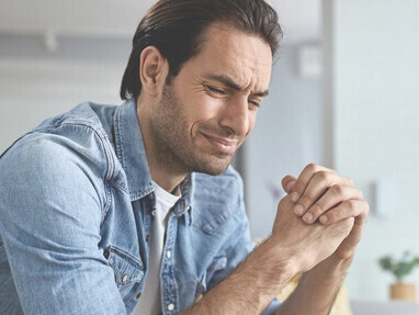 A young man sits alone at home, feeling depressed and overwhelmed by anxiety and stress