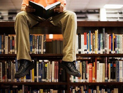 Un hombre leyendo sentado sobre una estantería