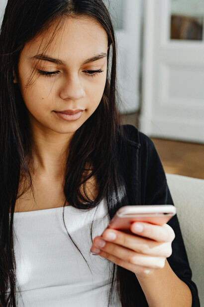 A woman in a black long-sleeved top uses her mobile phone while binge-watching a vertical series made up of short smartphone drama episodes
