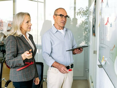 Two professionals examining plans on a whiteboard together, reflecting the value of reviewing progress before moving forward