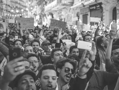 A black-and-white photo of a crowd protesting, many holding smartphones, Morocco