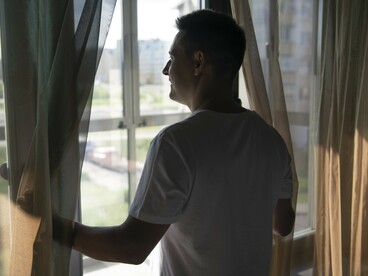 A man opens the curtains to the outside world, symbolizing the fragile boundary between safety and danger