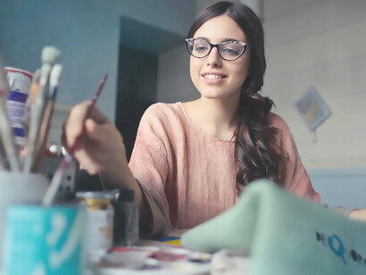 Woman painting at table full of paint brushes