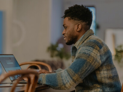 A focused Black man works on a laptop while drinking coffee in a café