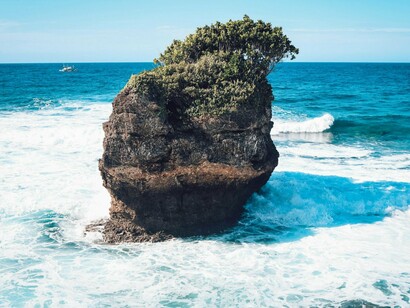 A lone rock formation surrounded by bright blue waters, symbolizing the enduring connection with nature in Davao, Philippines