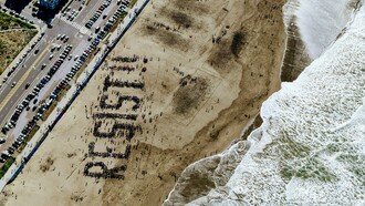 Aerial photo of a highway with the word “resist” written on the beach — symbolizing the tension between movement and stillness, and the human struggle between progress and resistance to change