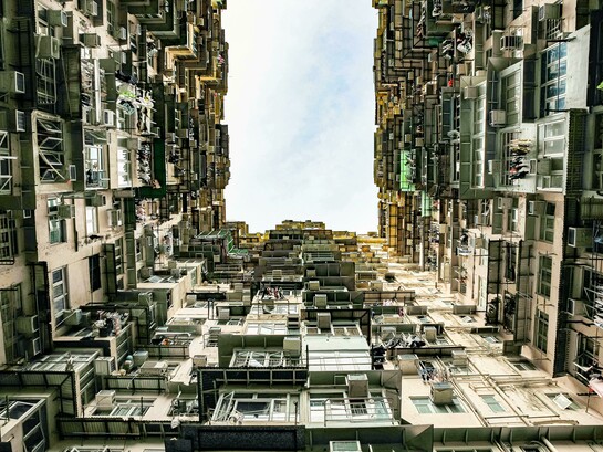 Low-angle view of a towering residential building in Hong Kong, reflecting the stark contrast between urban density, inequality, and poverty