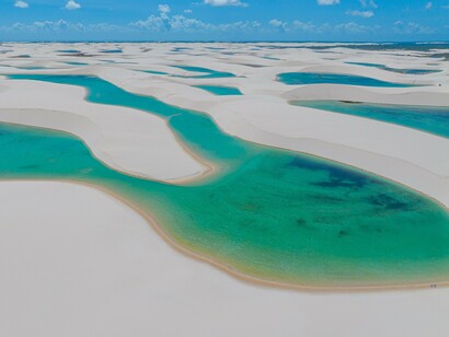 A vista aérea revela a vastidão da paisagem costeira, com bancos de areia clara e áreas de água que desenham formas irregulares. Diante de uma natureza tão grandiosa, a reflexão sobre a autossuficiência ganha outra dimensão: nem tudo está sob o nosso controle