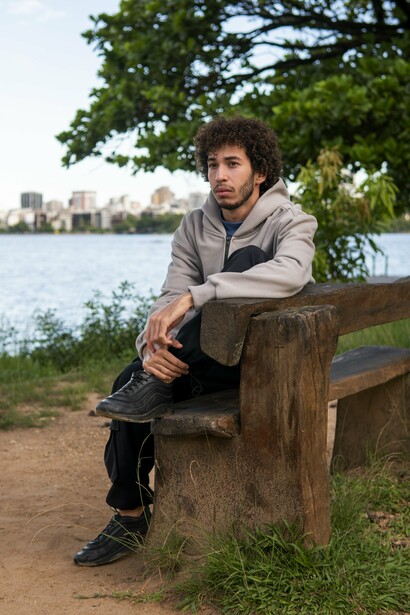 A young man retreating into himself while sitting alone outdoors, reflecting the tendency to push inward and shut others out before they can leave