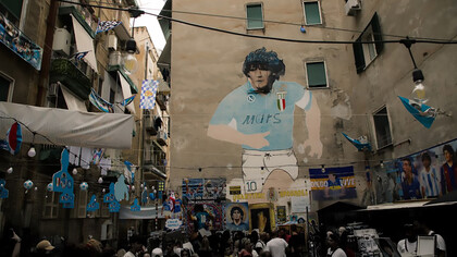 A large mural depicting a man wearing a helmet on the side of a building at Largo Maradona; Murales Maradona in Naples, Italy 