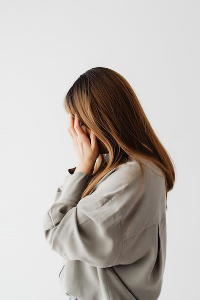 A demure woman dressed in gray long sleeves, her hands delicately covering her face in a shy gesture