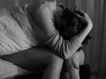 A person sits alone with a blanket, holding her head as she appears anxious and deep in thought