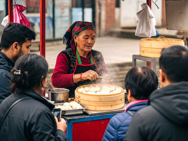 An elderly Nepali woman prepares and sells momos (traditional dumplings) at a small, colorful street food stall. Dressed in traditional attire with a vibrant headscarf, her face reflects years of experience as she tends to a steaming bamboo steamer filled with freshly made momos